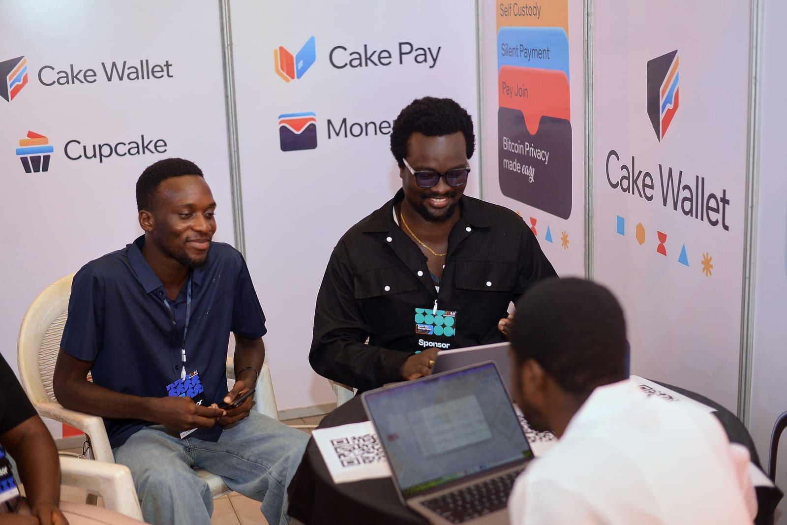David laughing at the Cake Labs booth with a laptop open, talking with two attendees.