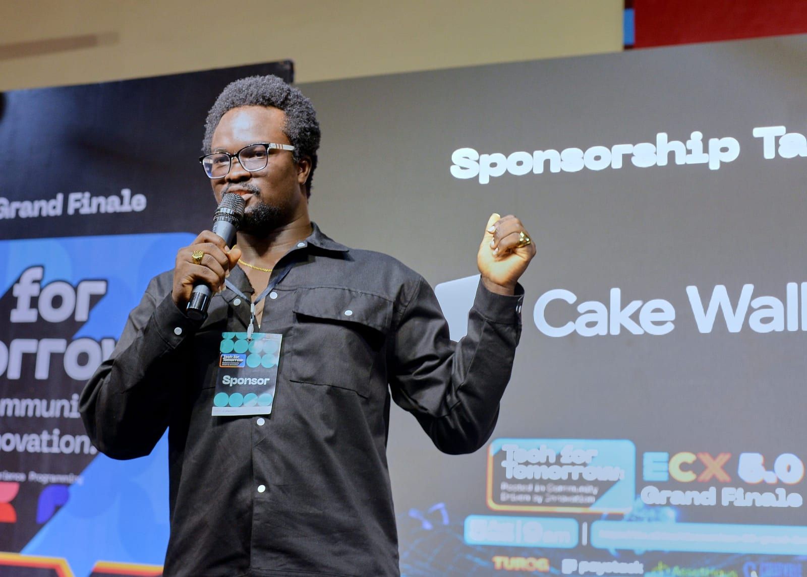 David speaking with a mic in one hand and a fist raised, Cake Wallet on the screen beside him.